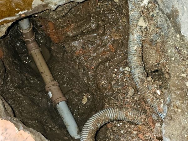 Vala aberta sob o piso com a tubulação e o eletroduto expostos no ponto do vazamento